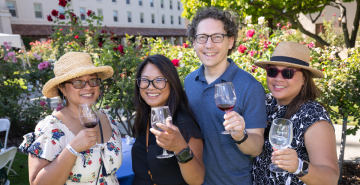 Three women and a man smiling and toasting the camera with wine glasses at the Vintage Santa Clara wine and food festival. 
