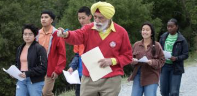 A person in a red sweater pointing, leading a group of people outdoors.