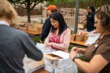 A woman in a Santa Clara University lanyard smiles as she packs toiletries for a nonprofit. Others helpers around her are slightly out of focus.