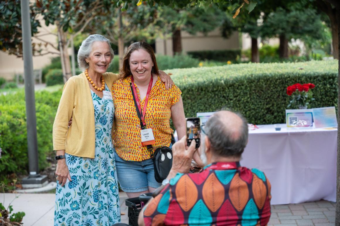 Two women posing as a man takes their picture on a cell phone at Santa Clara University's LGBTQ+ Alumni Social at Grand Reunion.