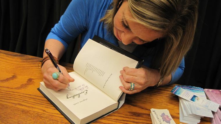 Woman author at a table signing a book