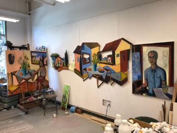 A studio with colorful paintings displayed on the wall.