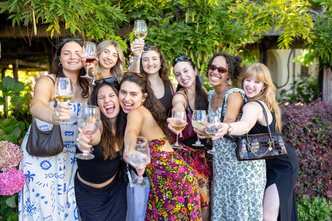 A large group of alumni cheersing the camera in front of the Wisteria Arbor in the Mission Gardens 