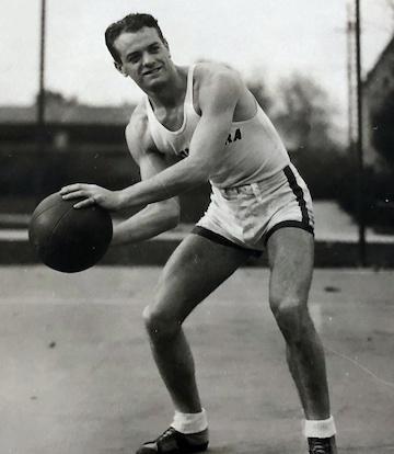 A black-and-white photo of a man playing basketball outdoors.