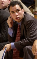 A man in a suit, sitting pensively.