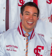 Man smiling in a white Hall of Fame jacket with red letters.