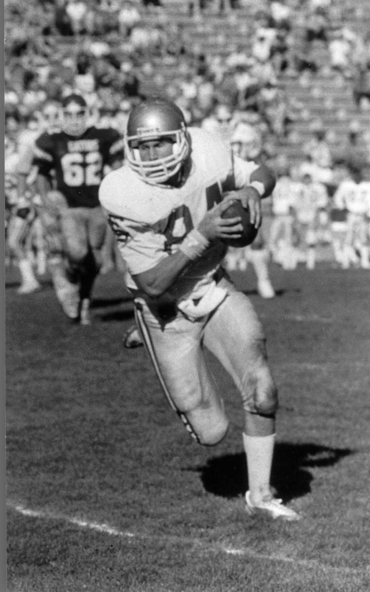 Football player running on field in uniform carrying the ball.