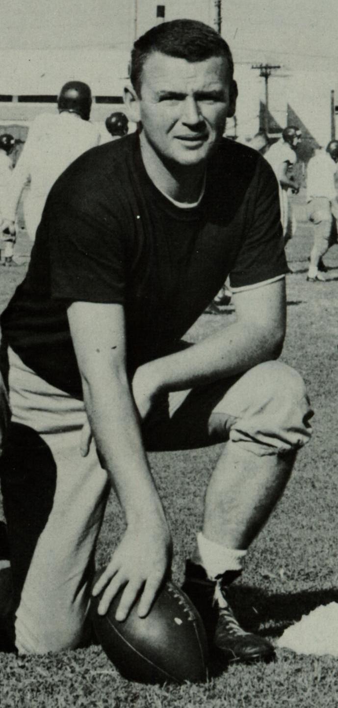 A person kneeling on one knee holding a football on a field.