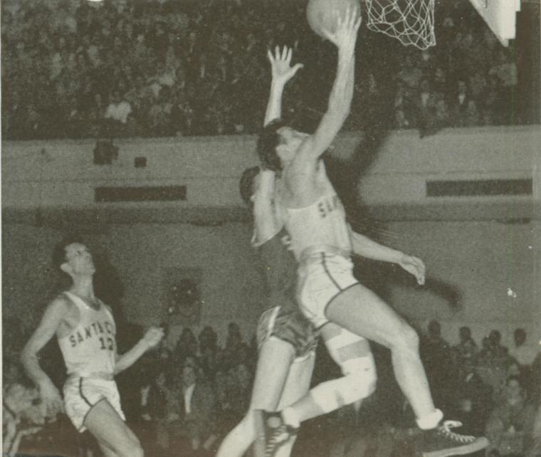 Black and white photo of basketball players in-game action, one shooting towards the hoop.