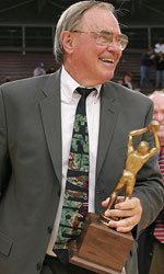 An older man holding a trophy, dressed in a suit.