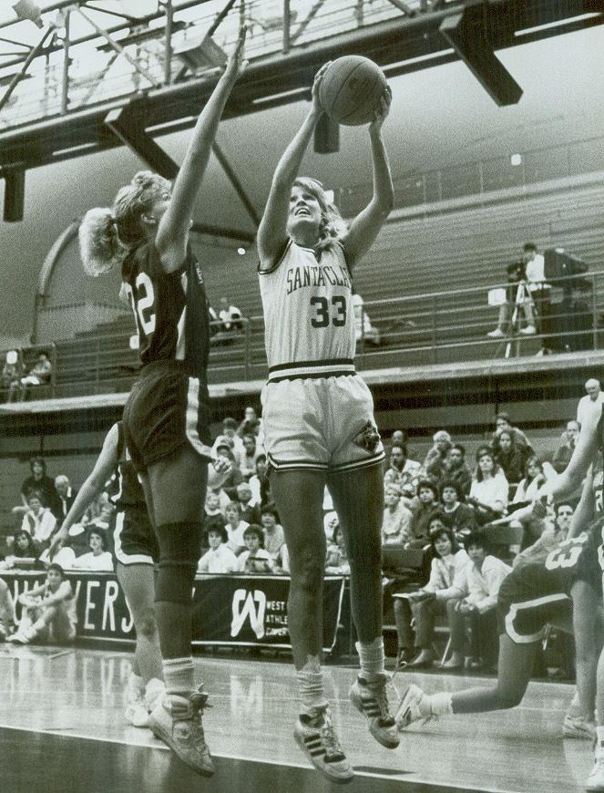 A basketball player shooting while a defender attempts to block the shot.