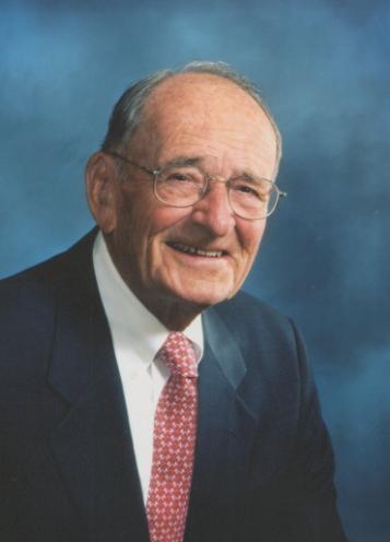 Man smiling in a suit with a pink tie and blue background.