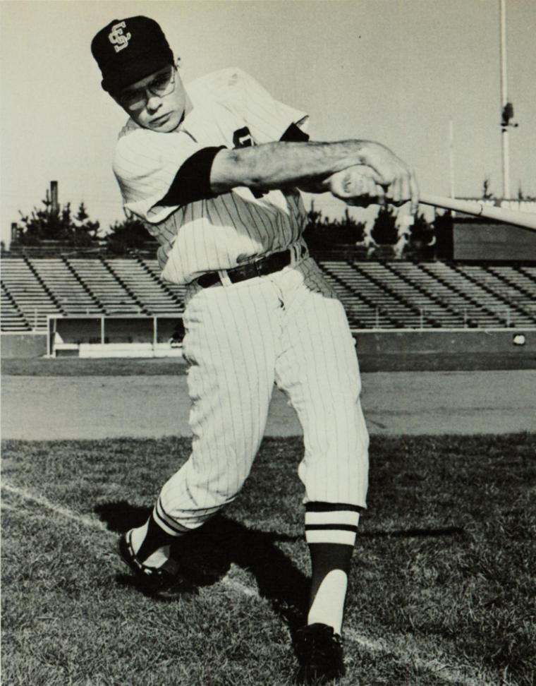 Baseball player swinging bat with determination on a field, background stadium seating.
