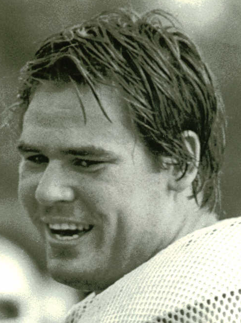 Black-and-white photo of a man smiling wearing football gear.