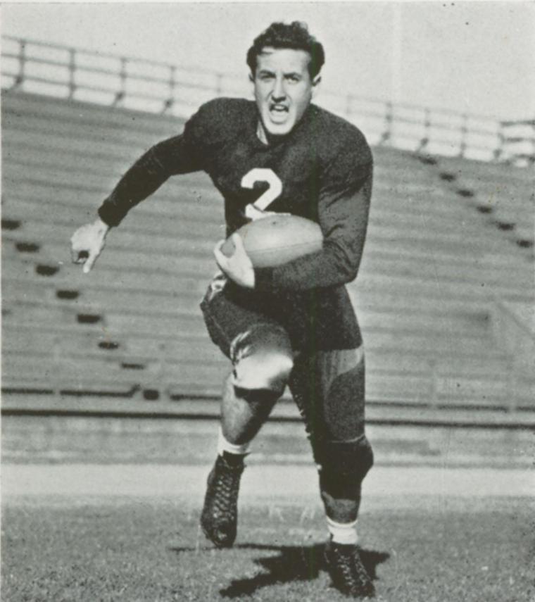 A football player running on a field holding a football in 1939.
