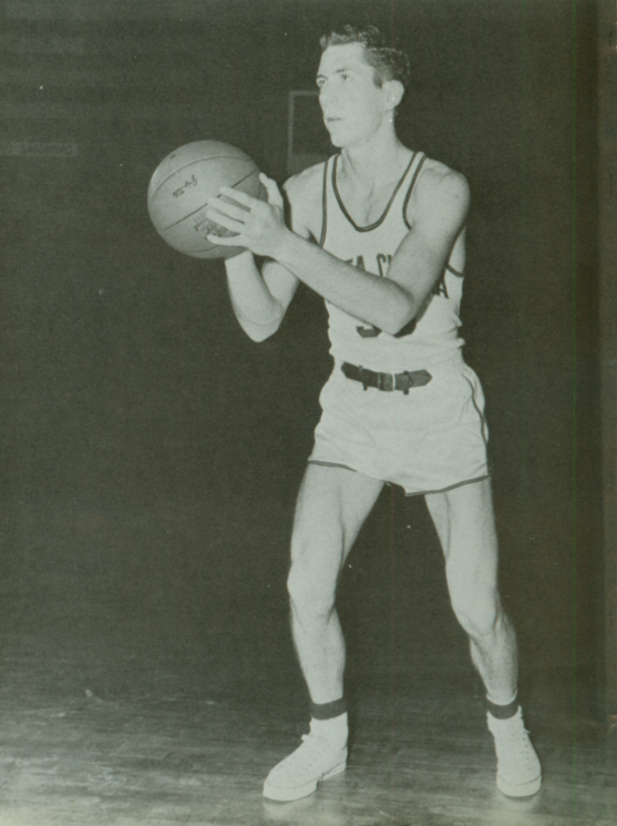 A basketball player holding a ball in a ready stance, circa 1960.