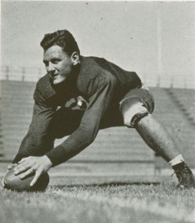 Football player in uniform crouching and holding a football. Image titled John Schiechl HOF.