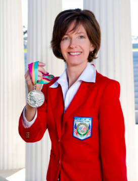 A person in a red blazer holding medals, smiling.
