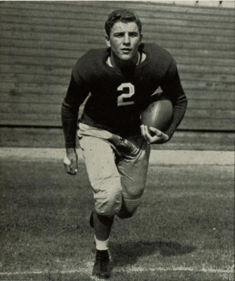 Black-and-white photo of a football player in a 1942 uniform holding a football.