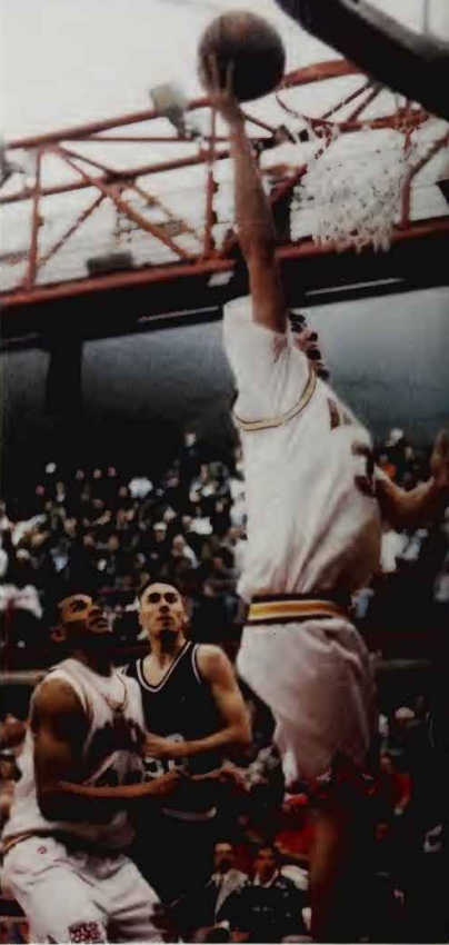 A basketball player dunking the ball during a game with opponents below.