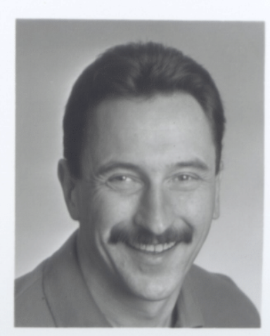 Black and white portrait of a man with a mustache smiling.