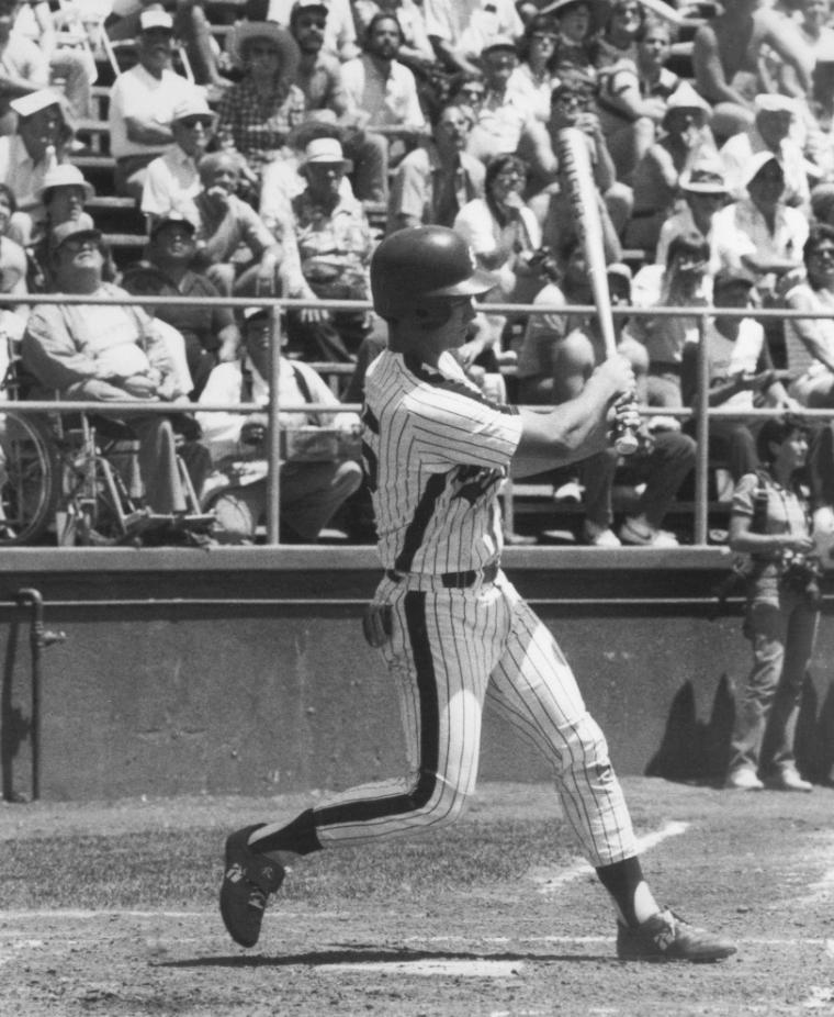 Baseball player mid-swing with a crowd in the background.