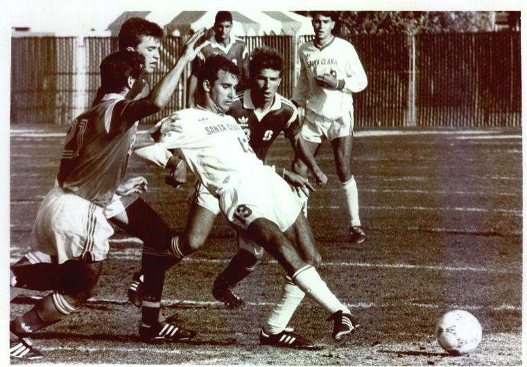Soccer players mid-action on field; one in white uniform (Paul Holocher).