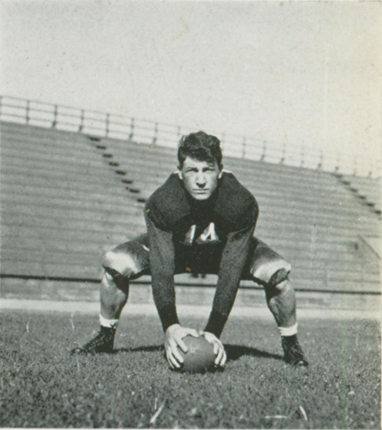 A football player crouches holding the ball in a stadium, 1938.