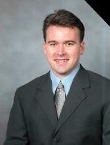 A man in a suit smiling in a professional photo.