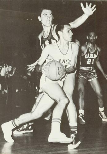 Two men playing basketball with one reaching to block a shot.