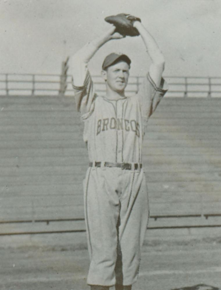 A vintage baseball player holding a ball above his head, wearing a uniform.