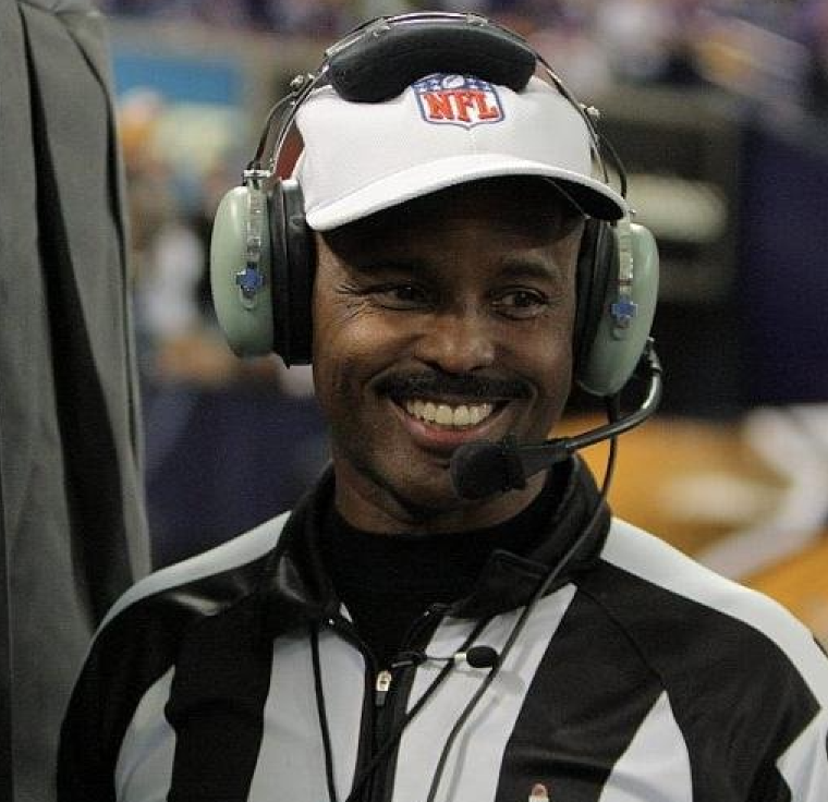 A smiling person wearing a referee uniform and headset.