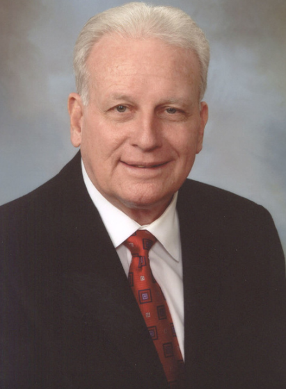 A man in a suit with a red tie smiles at the camera.