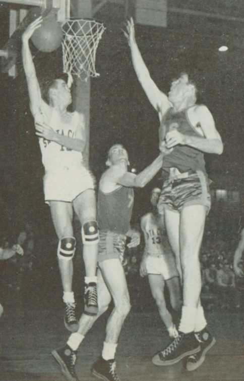 Three basketball players jump near the basket during a game.