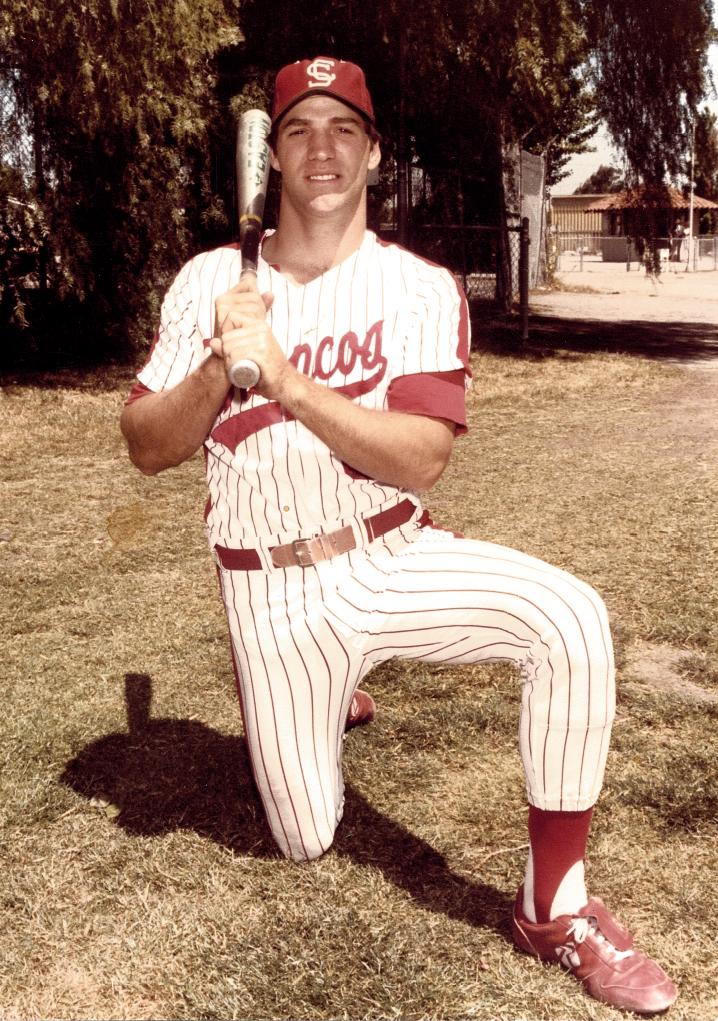A baseball player kneeling on a field with a bat.