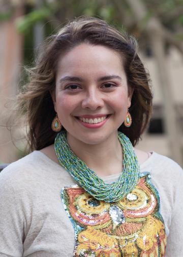 A person wearing a colorful necklace and decorated shirt, smiling at the camera. image link to story