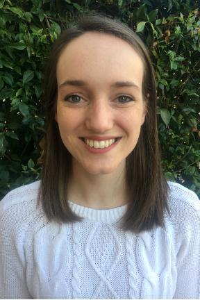 A person smiling, wearing a white shirt, with greenery in the background. image link to story