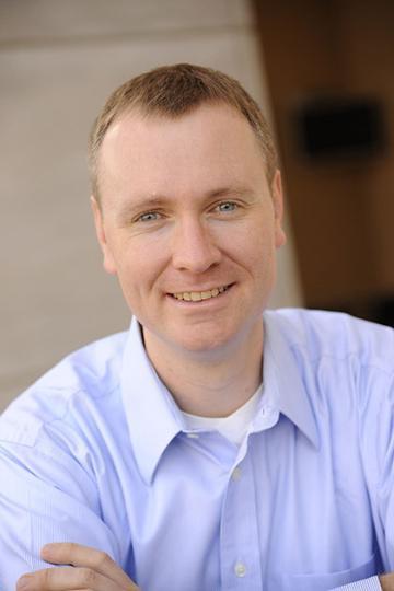 A person smiling, wearing a light blue collared shirt. image link to story