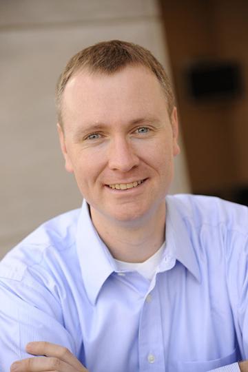 A person smiling, wearing a light blue collared shirt. image link to story