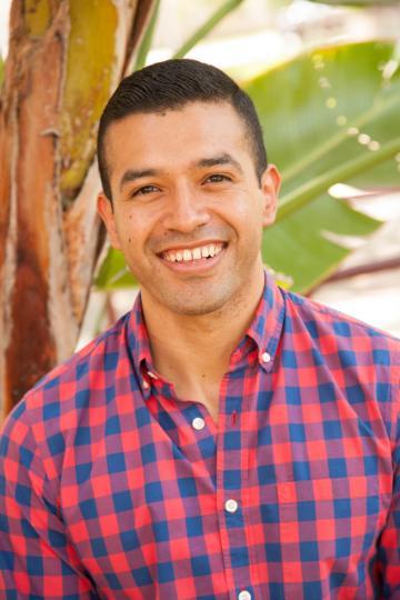 A person smiling in a checkered shirt outdoors.