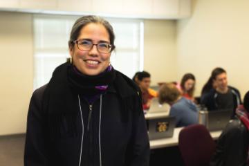 A person smiling in a classroom setting with seated people in the background. image link to story