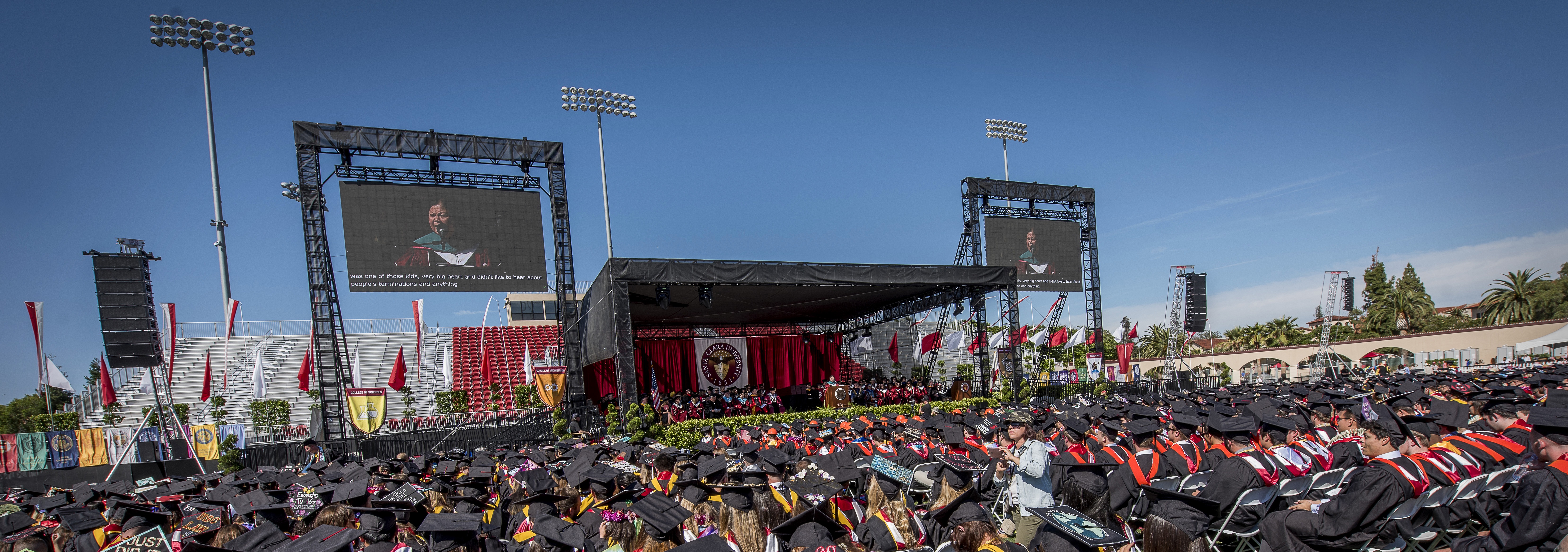 Large outdoor stage with a crowd at an undergraduate commencement ceremony.