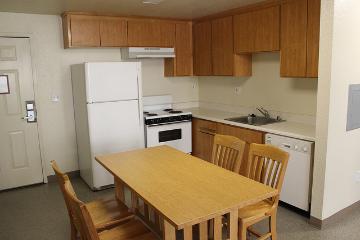 A tidy kitchen with wooden cabinets, white appliances, and a wooden dining table with chairs.