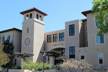 Sobrato Hall building with tower and arched entrances under clear blue sky.