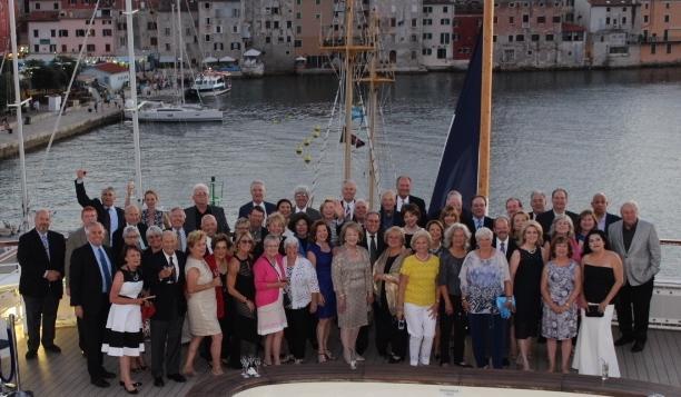 A large group of people posing by a harbor with boats.