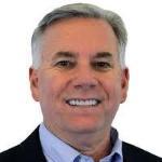 A man wearing a suit jacket, dress shirt, and smiling.