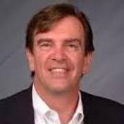 A man wearing a suit jacket and white shirt, smiling.