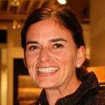 Smiling person in indoor setting with lights in the background.