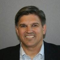 A person in a suit smiling in front of a gray background.