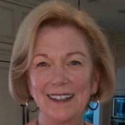 A smiling person wearing a necklace and a light-colored top.